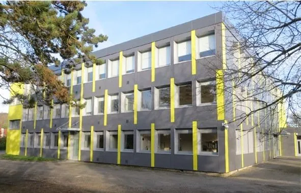 Bâtiment moderne gris et jaune, trois étages, fenêtres.